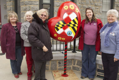 Harford Artists in front of Bel Air Armory surrounding a red heart sculpture with daisies and Maryland flag graphics