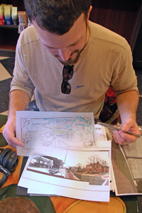 Marshall Adams sitting in Shamrock Coffee and showing the drawings he prepared before starting to paint the mural on the Sheriff's Office