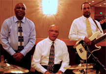 Three musicians dressed in shirts and ties; one sitting, others standing on either side