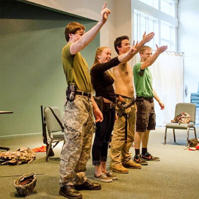 Four smiling young adults on a stage raise their right hands to audience